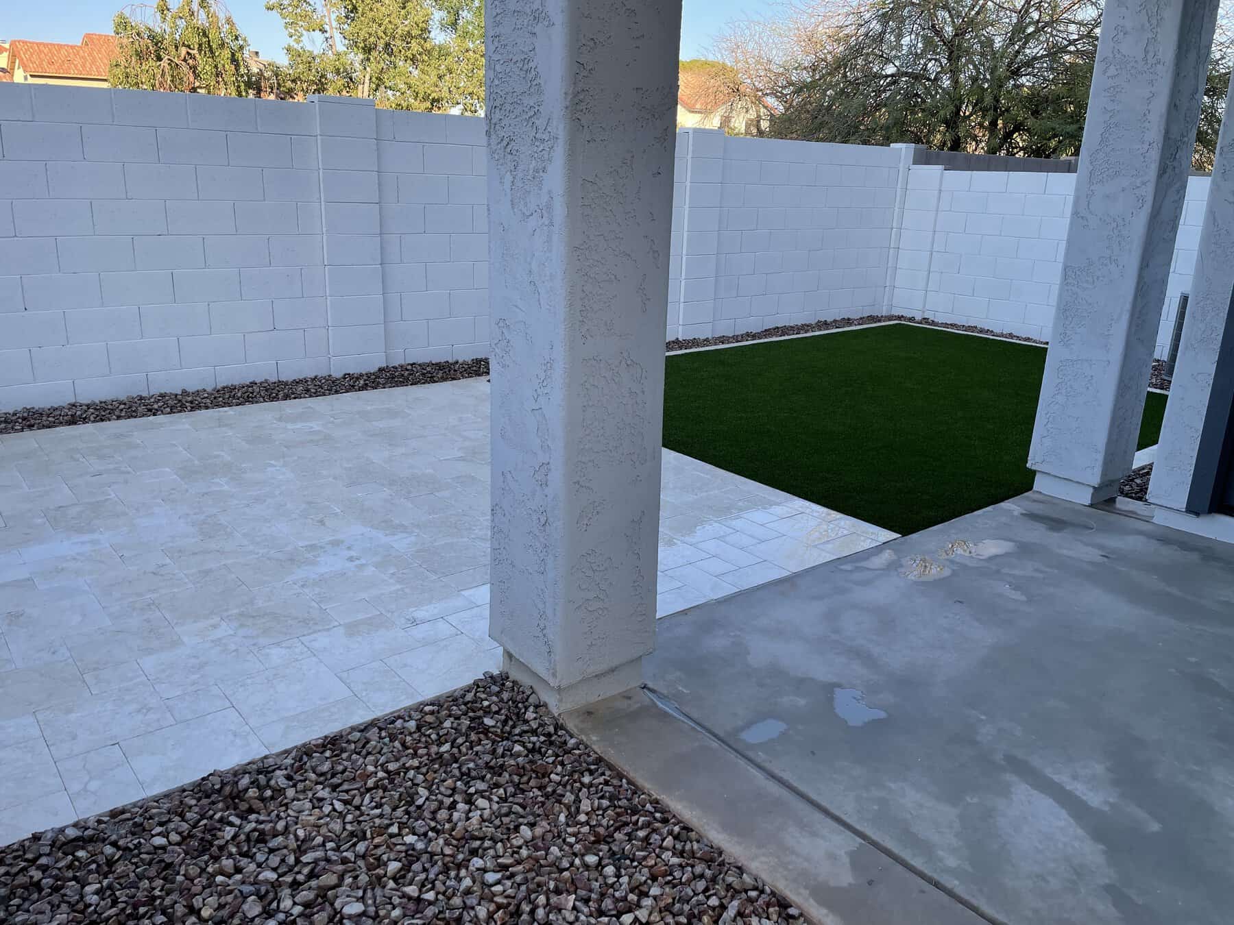 Enjoy a backyard retreat featuring a concrete patio, white stucco pillars, artificial grass, tiled flooring, and white brick walls. Landscaping rocks line the edges—expertly crafted by your trusted Pavers Installer Texas.